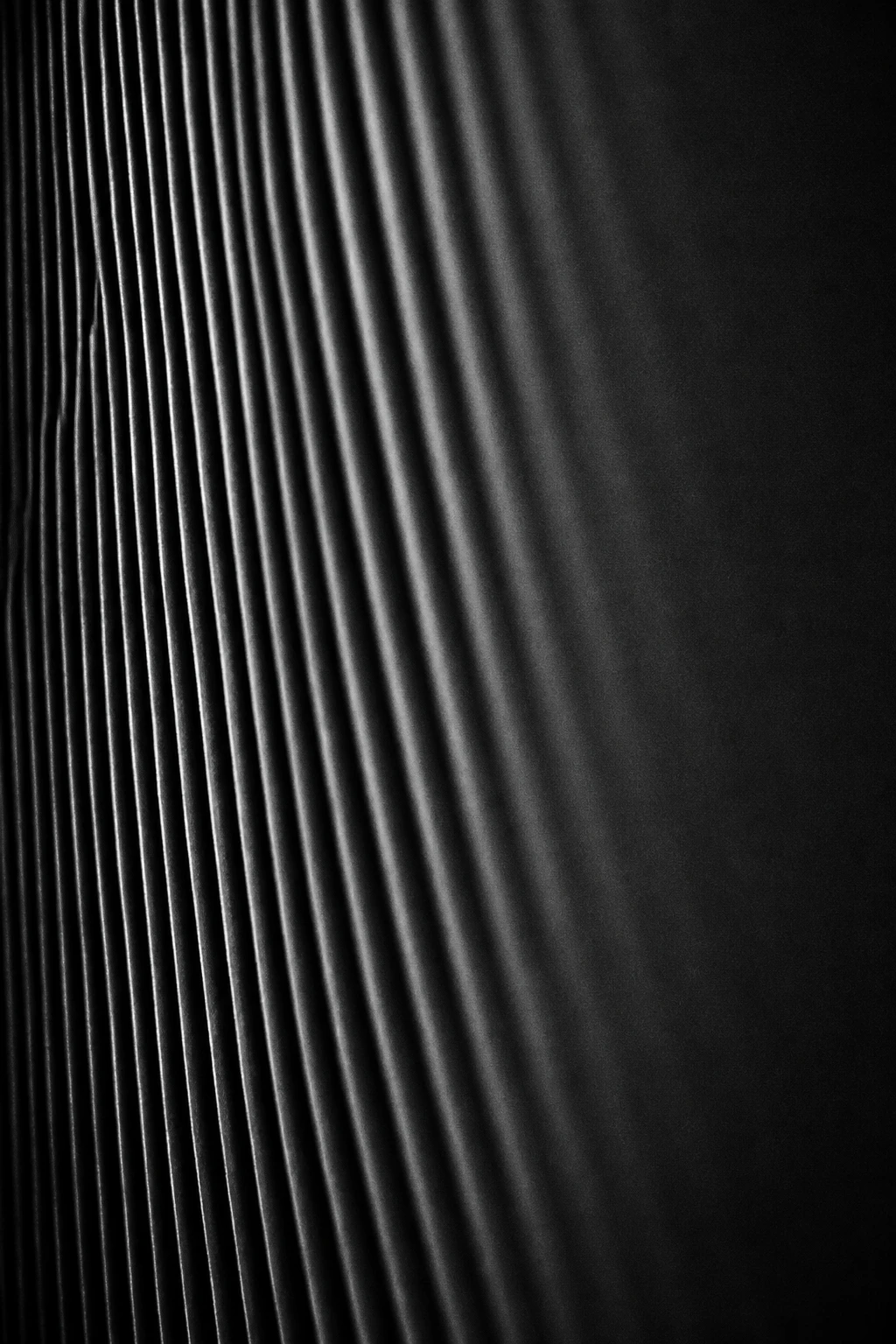 Closely spaced vertical pleats fading from lit on the left into darkness on the right